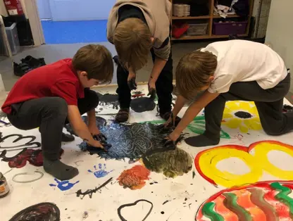Three boys creating a large finger painting on the floor